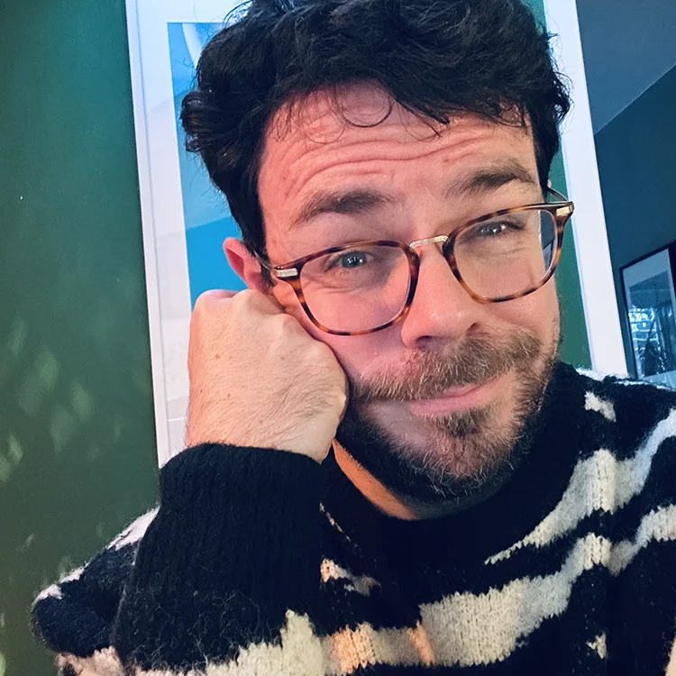 Porträt von Boris Jakob, Grafikdesigner, nachdenklicher Gesichtsausdruck vor grünem Hintergrund. Thema: Sprachtrends, Füllwörter und bewusste Kommunikation im Arbeitsalltag.